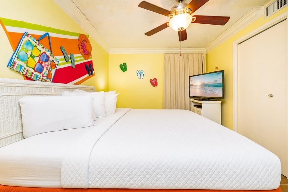 Brightly colored decor complements the spacious bedroom featuring a large king bed, a ceiling fan, and a flat-screen TV