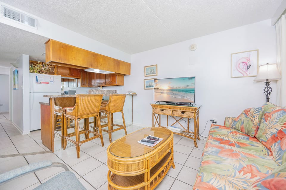 Living area featuring tropical decor, a flat-screen TV, and a cozy rattan seating arrangement with queen sofa-sleeper