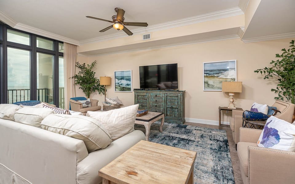 This inviting living area features a large TV, plush seating, and a beautiful beachfront view framed by expansive windows