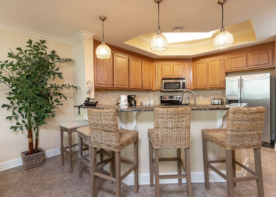 This kitchen features wood cabinetry, stainless appliances, and a breakfast bar with stylish wicker stools for casual dining