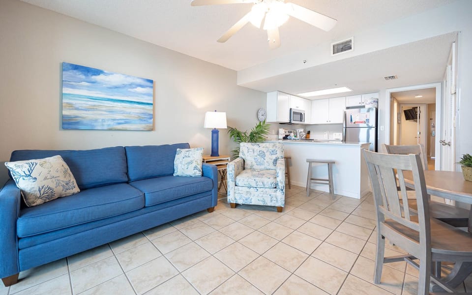 Relax in the airy living area with a blue sofa, patterned chairs, and a view of the kitchen and dining space nearby