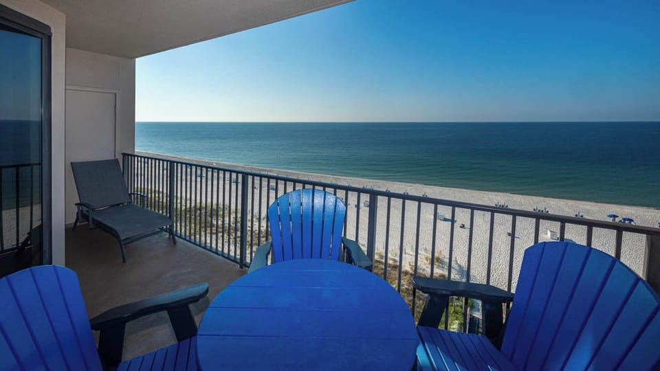 Relax in vibrant blue chairs on the balcony, enjoying expansive views of the tranquil water and beach below