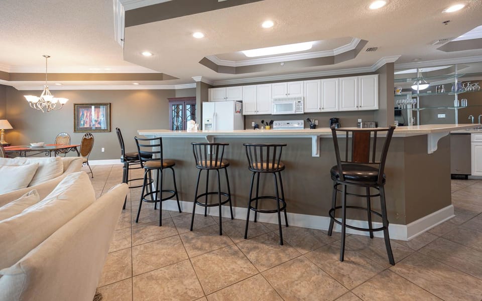 Kitchen bar area with stylish bar seating, a kitchen featuring white cabinetry and appliances and spacious countertops