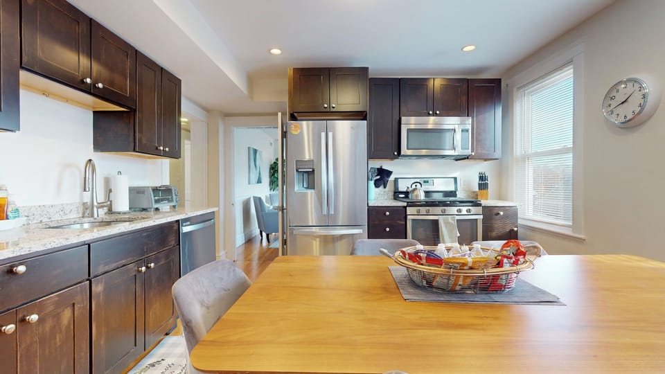 Modern kitchen with sleek dark cabinets, stainless steel appliances, granite counters, and a spacious dining table.