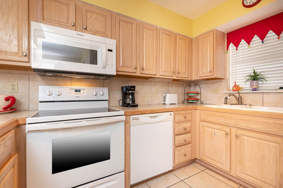 This kitchen features light wood cabinetry, essential appliances, and a sunny atmosphere, perfect for meal preparation