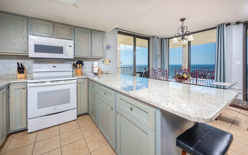 Bright coastal kitchen features light blue cabinetry, a spacious breakfast bar, and panoramic views of the beach front