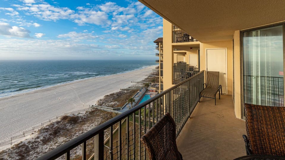 The balcony offers a serene view of the beach with white sand, complemented by comfortable seating for relaxation