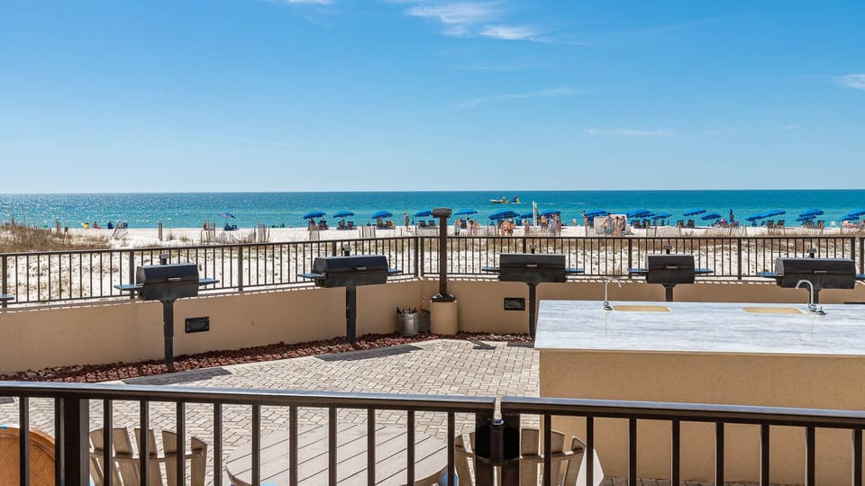 Enjoy grilling in the outdoor pool area, overlooking the beach and vibrant umbrellas on the shore