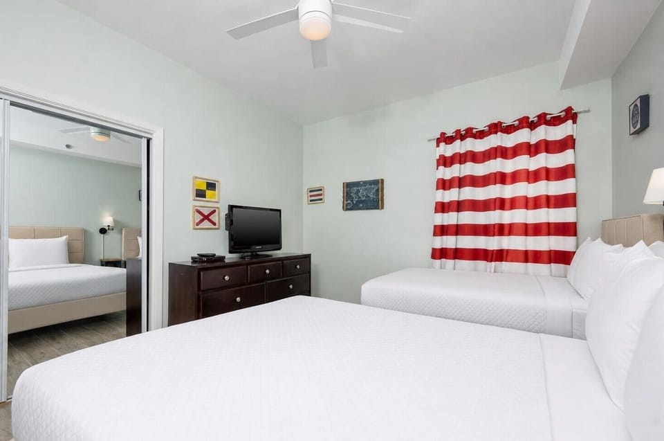 This guest bedroom features two beds, a queen and twin, a TV, and bright red striped curtains