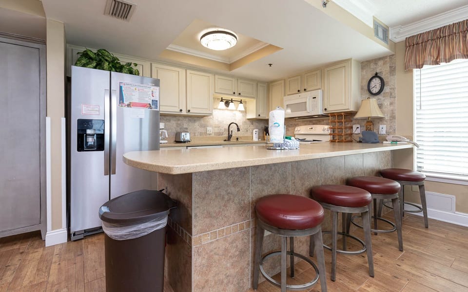The kitchen features stainless and white appliances, spacious countertops, and bar seating, perfect for dining with family