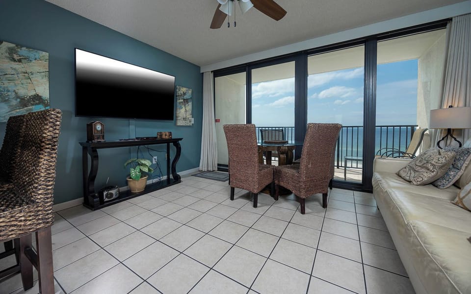 The inviting living area features a large TV and a dining table with a stunning beachfront view through expansive glass doors