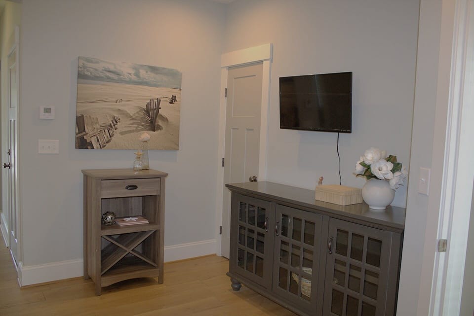 This is another angle of the first-floor king bedroom, showcasing a mounted TV, stylish storage cabinets, and coastal-themed décor.