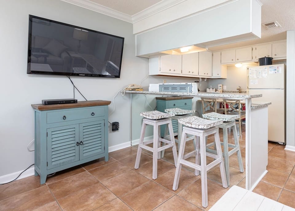 The space features a stylish seating area with a large TV and a well-equipped kitchen, perfect for relaxing and dining