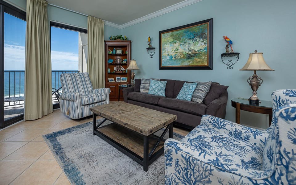 Living area features a sofa with queen sleeper, a striped chair, and stunning views of the gulf through large windows
