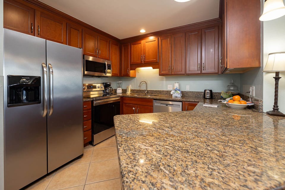 Wood cabinetry complements the granite countertops in this modern kitchen, featuring essential appliances and a fruit bowl