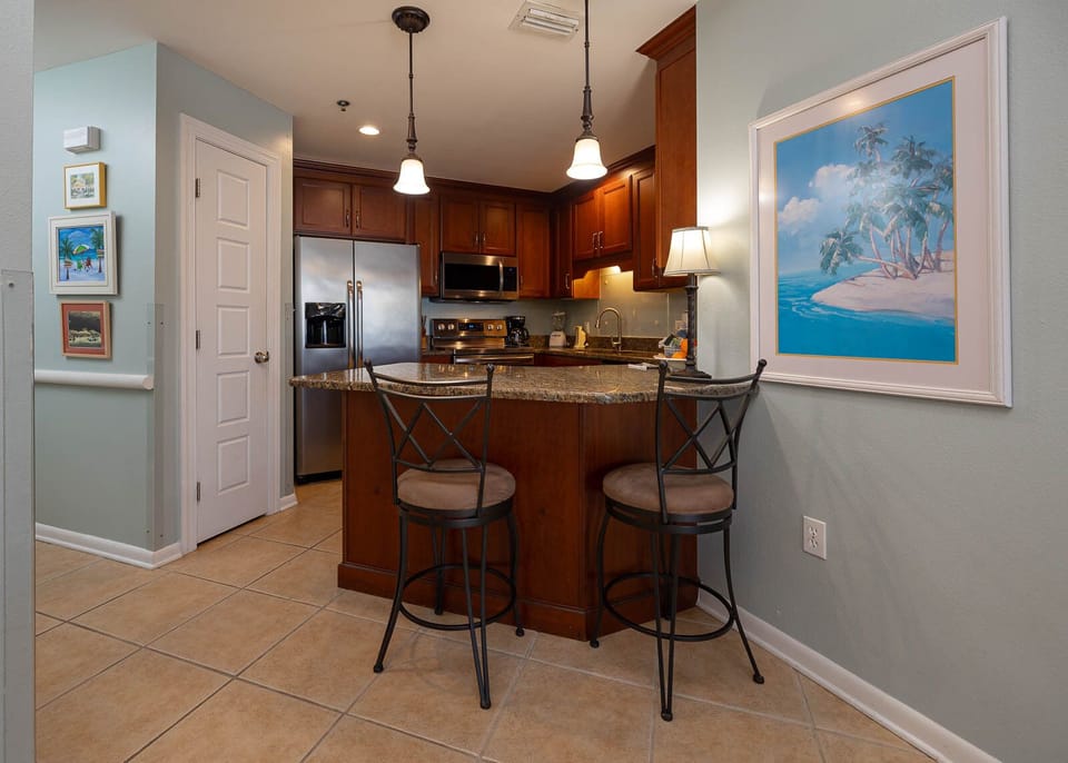 Modern kitchen area features dark wood cabinetry, granite countertops, and a breakfast bar with two stylish stools