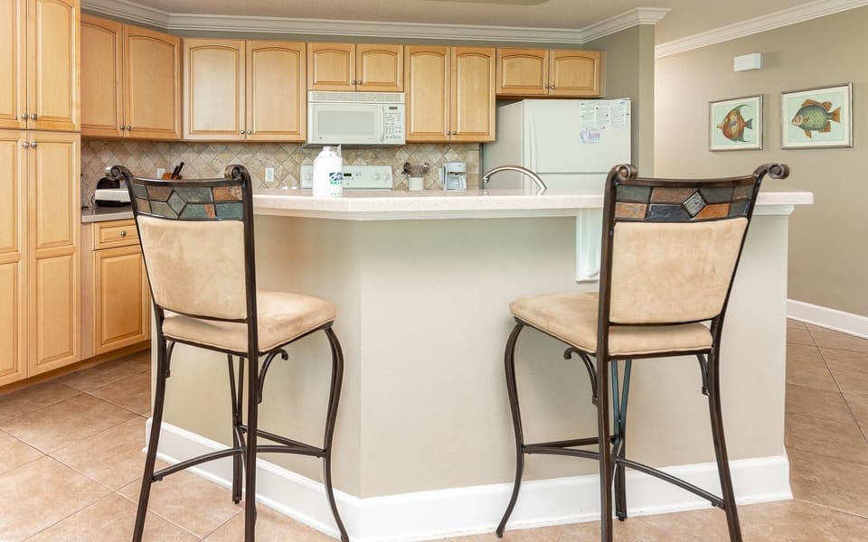 Kitchen featuring light wood cabinets, a breakfast bar with two stools, and colorful fish artwork