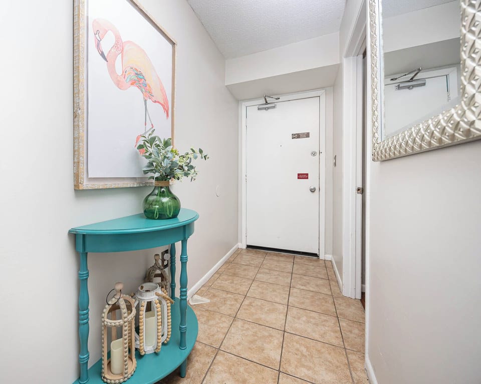 This welcoming entryway features a vibrant turquoise table, decorative lanterns, and a cheerful flamingo artwork