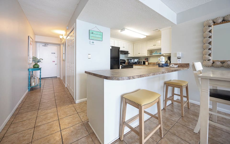 This kitchen features sleek black appliances, a breakfast bar with yellow stools, and a welcoming entryway with coastal decor