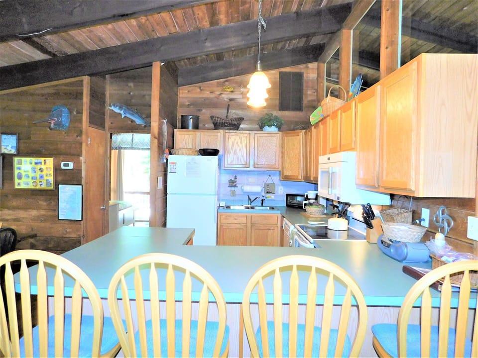 19 Addy Road - Sun-Filled Coastal Kitchen - This spacious kitchen offers ample counter space and a large breakfast bar with seating for four. Wood cabinetry and bright white appliances complement the home's warm and inviting cottage aesthetic.