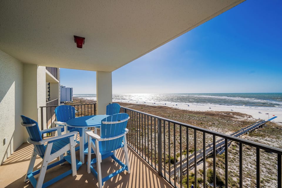 Bright blue chairs surround a circular table on the balcony, offering a stunning view of the glistening gulf and beach below