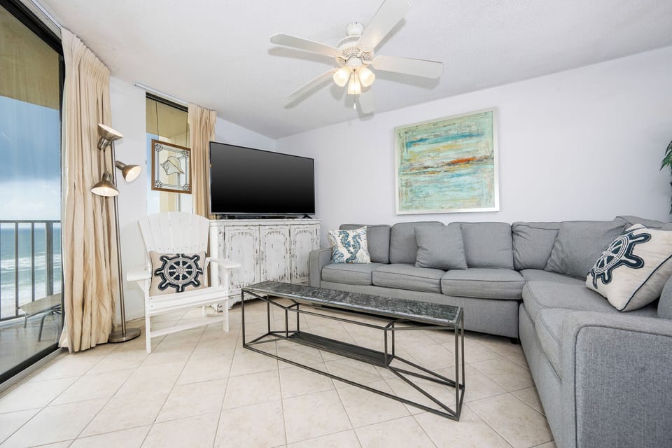Living area features a gray sectional sofa with queen sleeper, a decorative coffee table, and a view of the beach