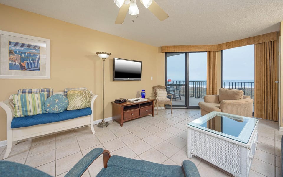 Cozy living area features a blue sofa with queen sleeper, a TV, and access to a balcony with a view of the gulf