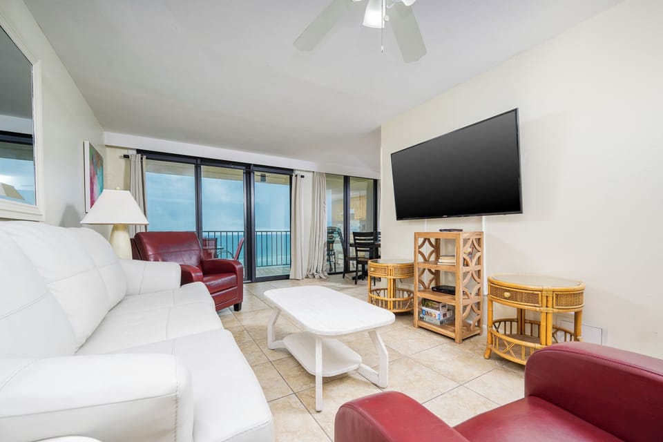 This living area features a large TV, cozy white and red seating, queen sofa-sleeper, and a beautiful view of the beach