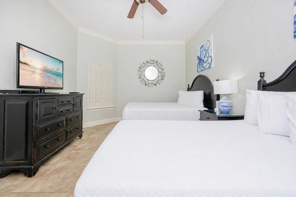 Bright and inviting guest bedroom featuring two queen beds, a flat-screen TV, and coastal-inspired decor
