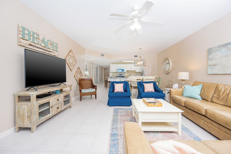 Unwind in the inviting living area with comfortable seating, a large TV, and a welcoming beach-themed decor