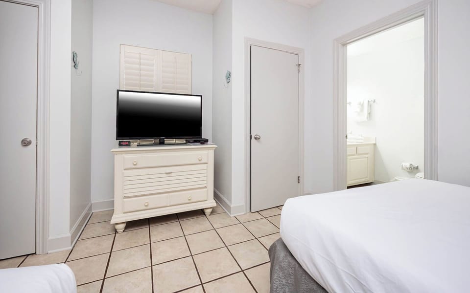 Bright guest room featuring a TV on a white dresser and an adjoining bathroom, offering a cozy retreat for relaxation