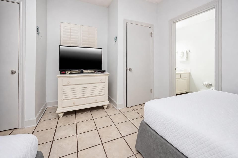 Bright guest room featuring a TV on a white dresser and an adjoining bathroom, offering a cozy retreat for relaxation