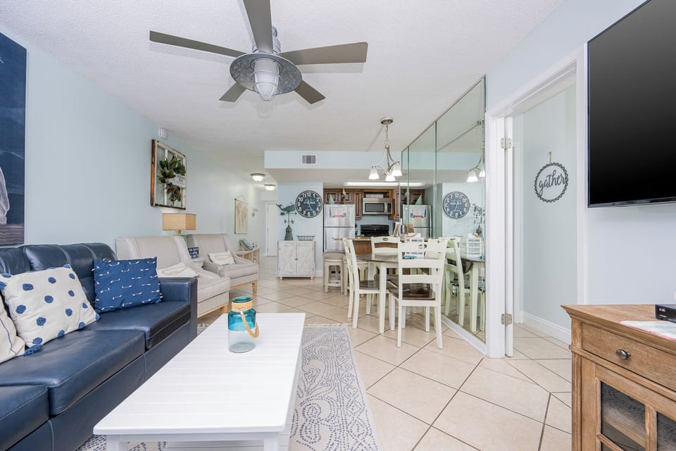 The living area features a blue leather sofa, a mounted TV, and a dining space with a mirrored wall, perfect for gatherings