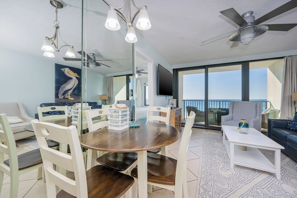 This inviting living area features a cozy dining table, a large TV, and stunning beachfront views through sliding glass doors