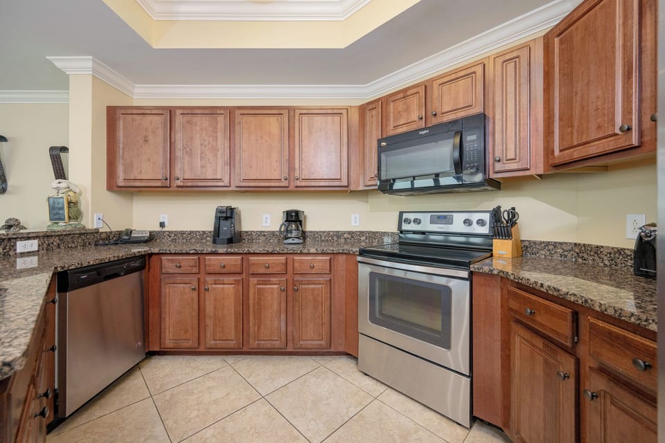 Kitchen featuring stainless appliances, rich wood cabinetry, coffee station, and granite countertops for a delightful stay