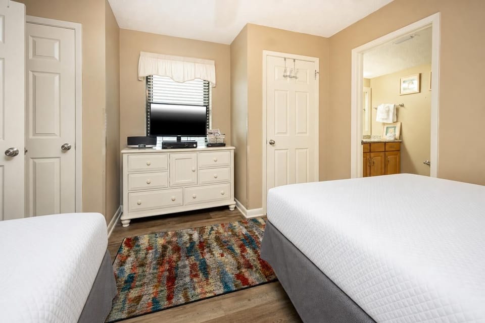 Brightly colored area rug complements two beds and a dresser with a TV, creating a welcoming guest bedroom atmosphere
