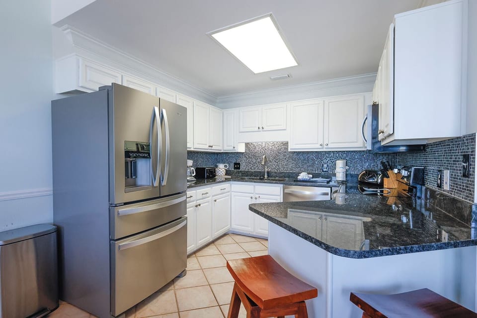 Bright kitchen features sleek cabinetry, a granite countertop, and a breakfast bar with seating, perfect for casual dining