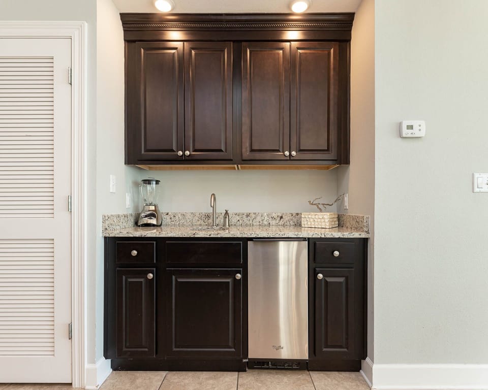 Enjoy preparing drinks at the stylish wet bar with dark cabinetry, blender, ice maker, and granite countertops