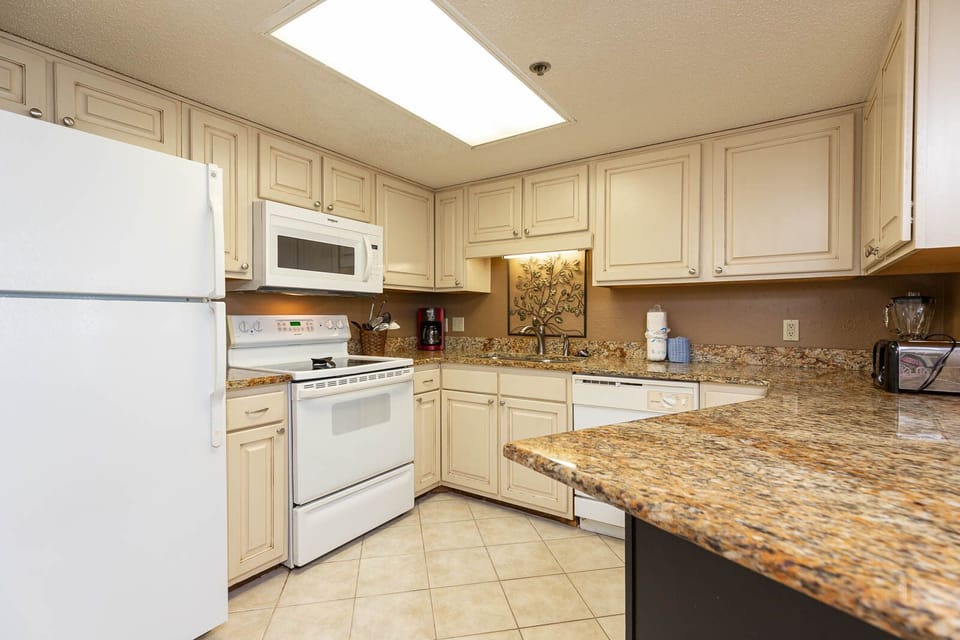 This kitchen features cream-colored cabinetry, a granite countertop, and a convenient breakfast bar