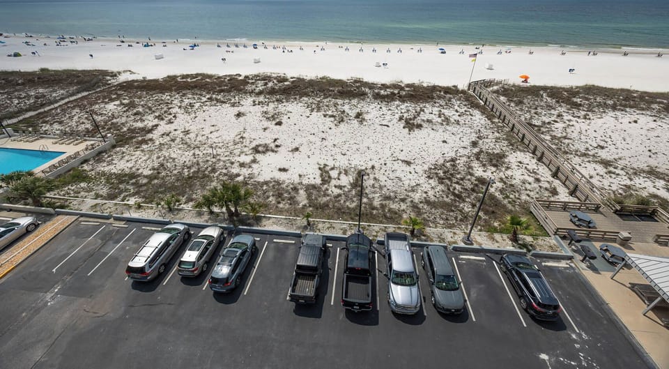 This view showcases a serene beachfront with white sand and beachgoers, complemented by a nearby inviting swimming pool