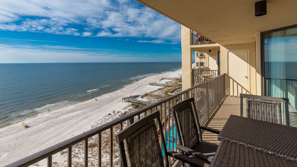 The balcony features stylish seating with panoramic views of the tranquil beach and gentle waves lapping at the shore