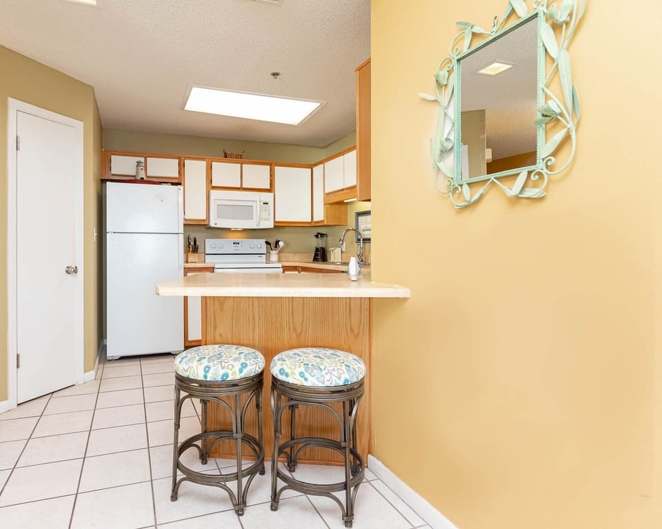 Bright kitchen area featuring a breakfast bar with stylish stools, ample cabinetry, and white appliances