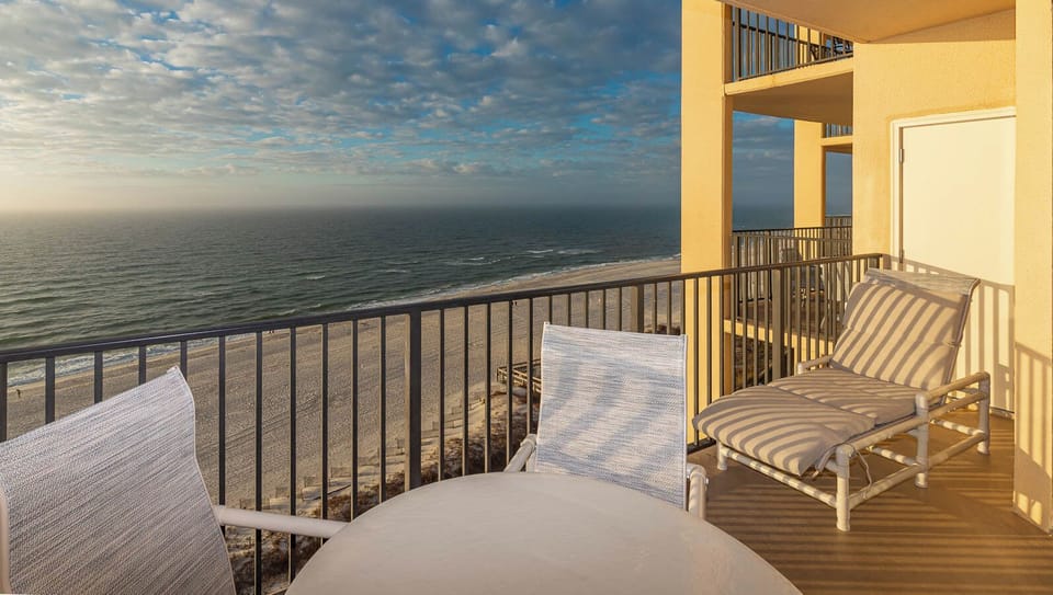 Enjoy a peaceful moment on the balcony with two lounge chairs and a table overlooking the tranquil beach and water