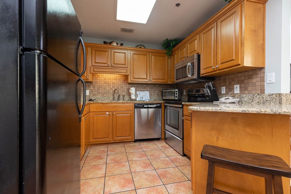 The kitchen features warm wood cabinetry, granite countertops, stainless appliances, and a breakfast bar with seating