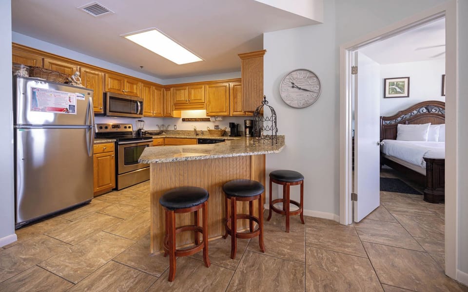 The kitchen features warm wood cabinetry, a granite countertop breakfast bar with seating, and a view into the master bedroom