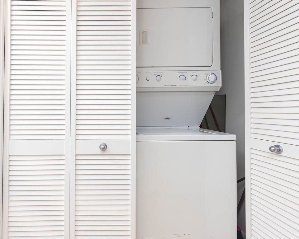 A stacked washer and dryer are neatly tucked behind louvered doors, providing convenient laundry access in the unit