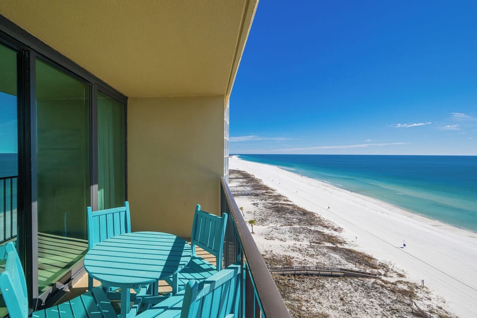 Sunlight sparkles on the coastline as you watch lively beachgoers from your balcony
