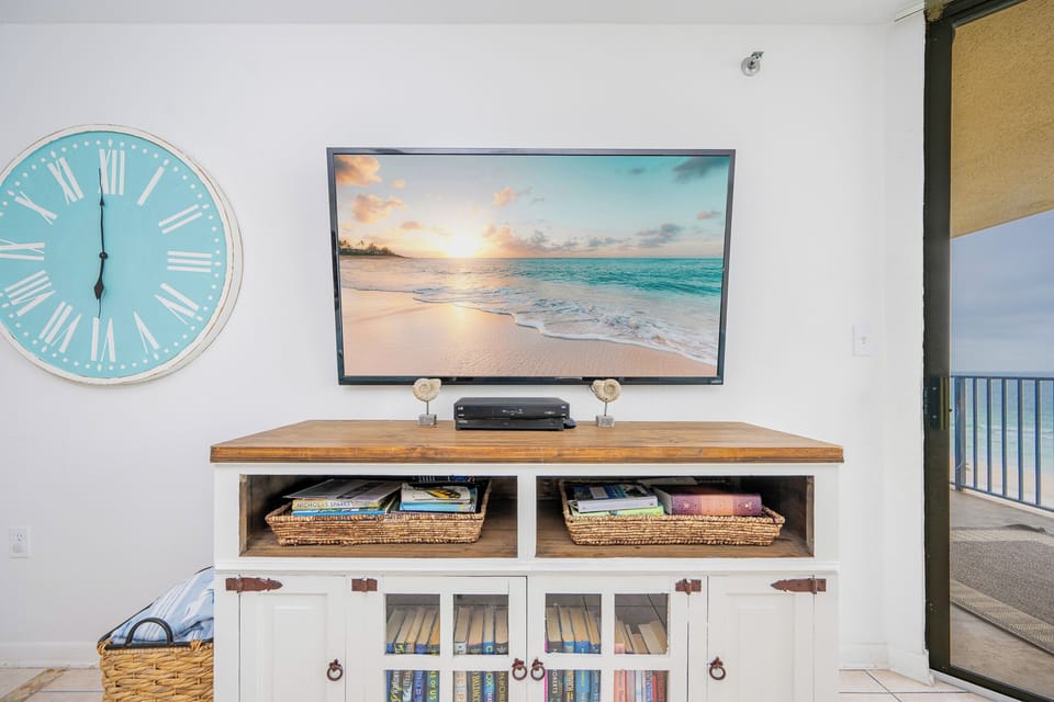 Books and beachy decor set a cozy mood as you get lost in a movie in the guest suite with queen bed