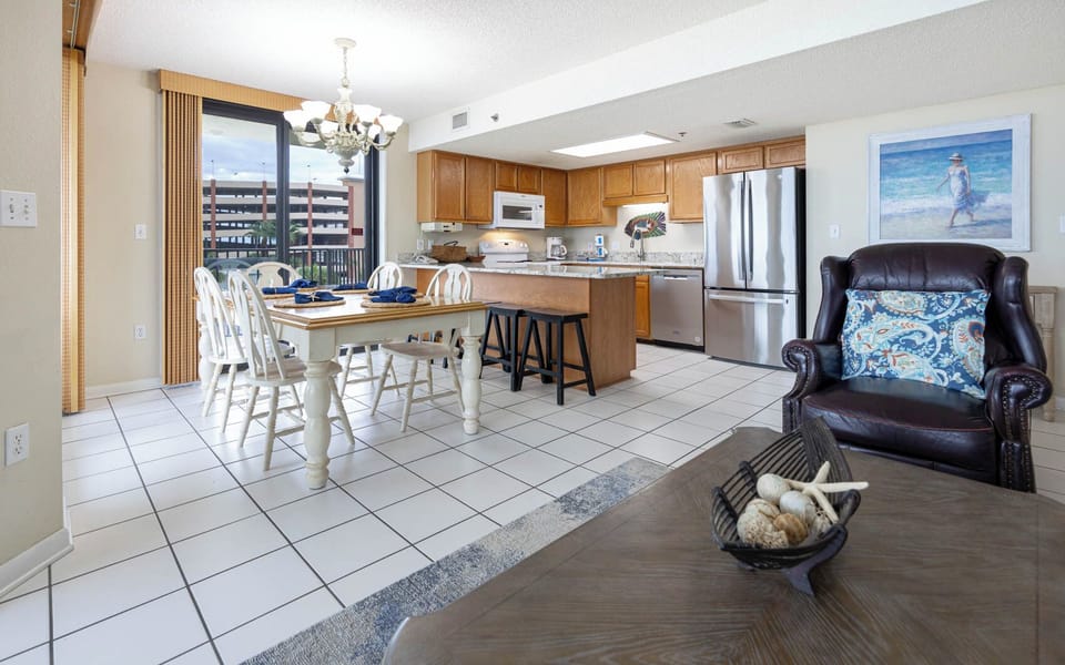 Bright dining area features a wooden table set for five, with a cozy leather chair and a modern kitchen in the background