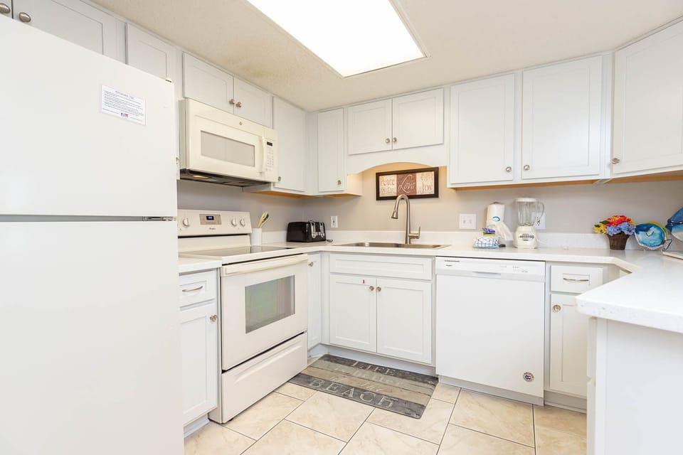 Bright white cabinetry and a cheerful beach-themed mat enhance this kitchen with white appliances and ample counter space